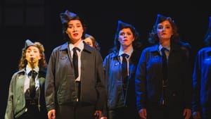 Maubach stands with several other women, all costumed as WWII service members, with solemn expressions under blue light.