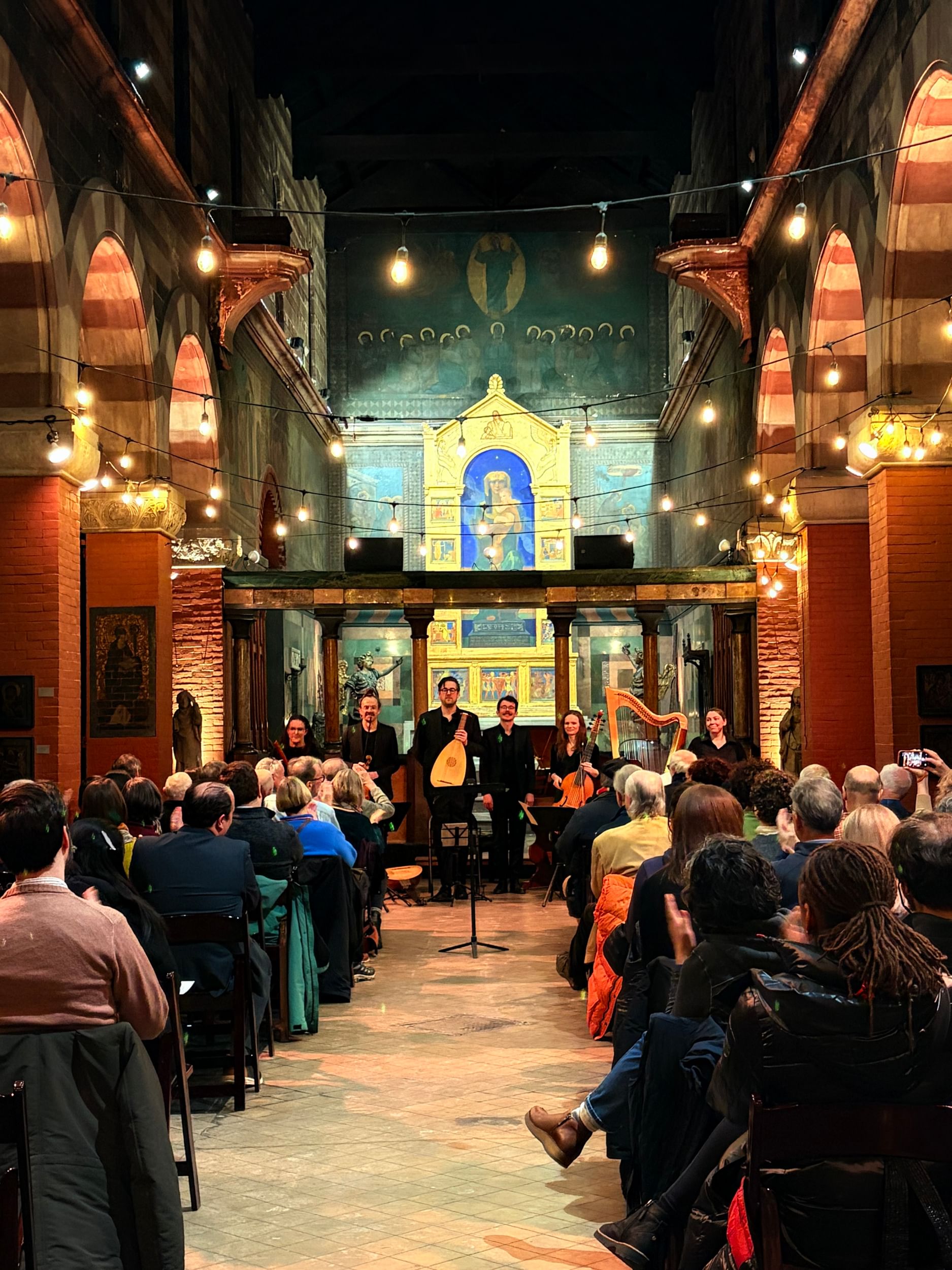 View of musicians on the chancel in a beautifully lit sanctuary space with classical and art deco vibes, and a full audience.