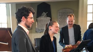 Candid photo of the musicians chatting onstage with approaching fans, instruments and music books around them.