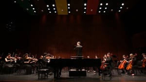 Ciabatti centered at a concert hall stage, several players to his left and right in black formal wear