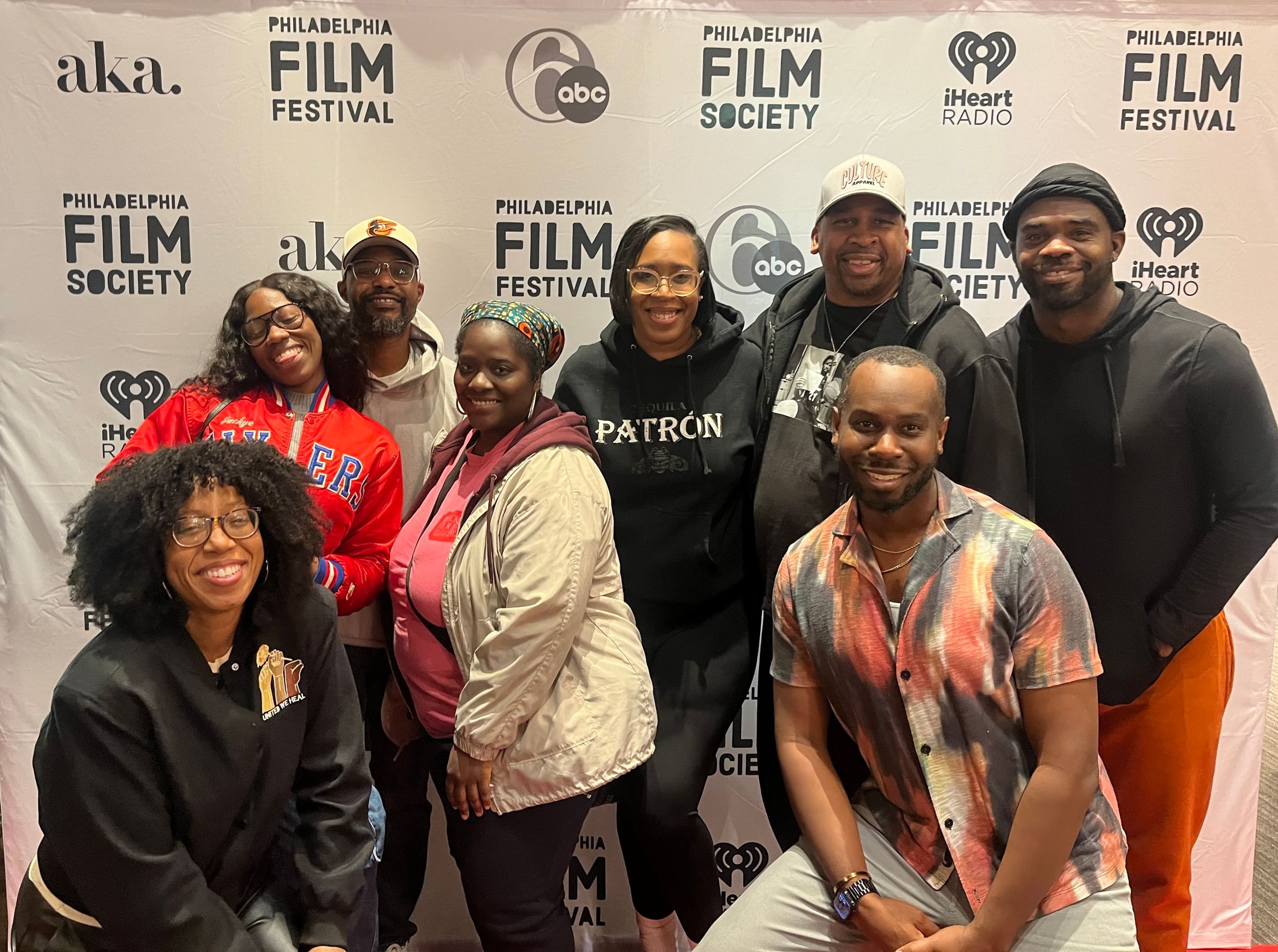 Eight smiling Black people wearing casual clothes pose together against a white Philly Film Festival backdrop.