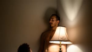 Grinberg, on his knees, faces the shirtless Header in a moment of sexual tension, next to a single lamp.