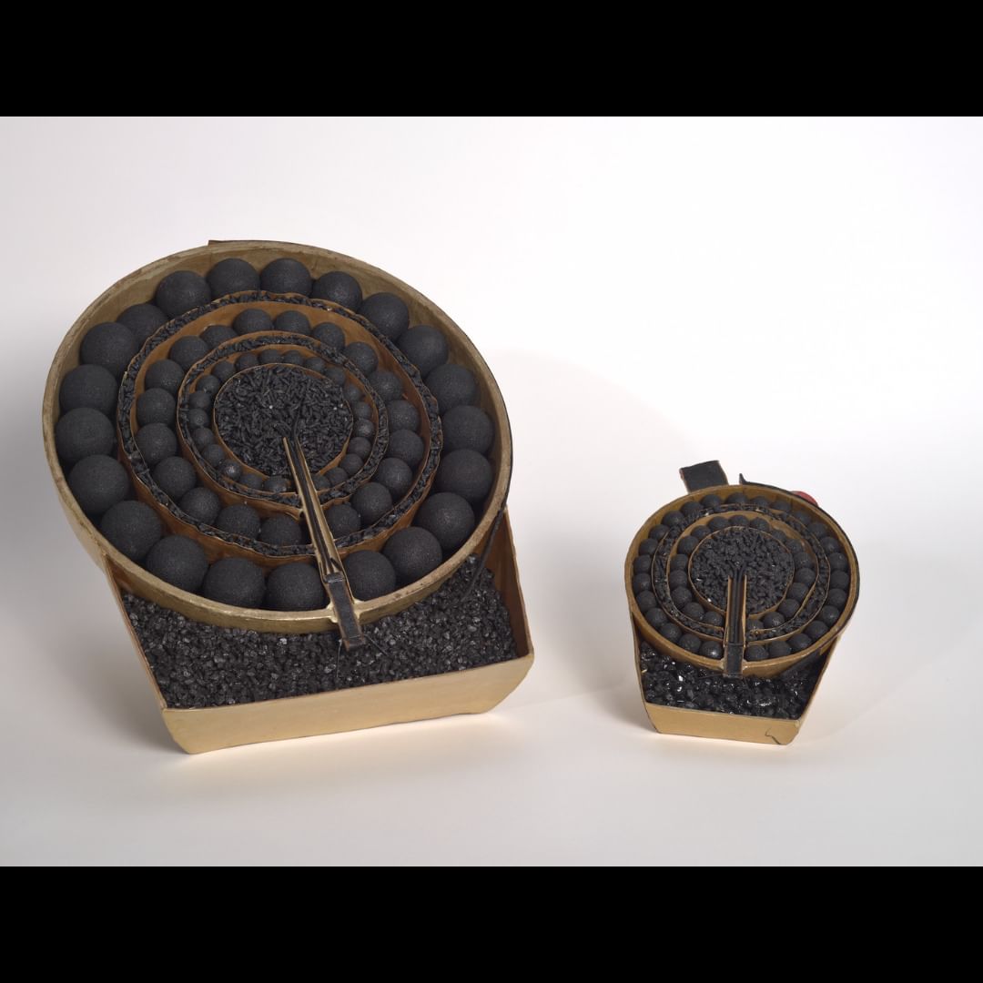 Black explosive materials, gravel-like or in small black balls, in concentric circles in a brown case with a fuse at bottom