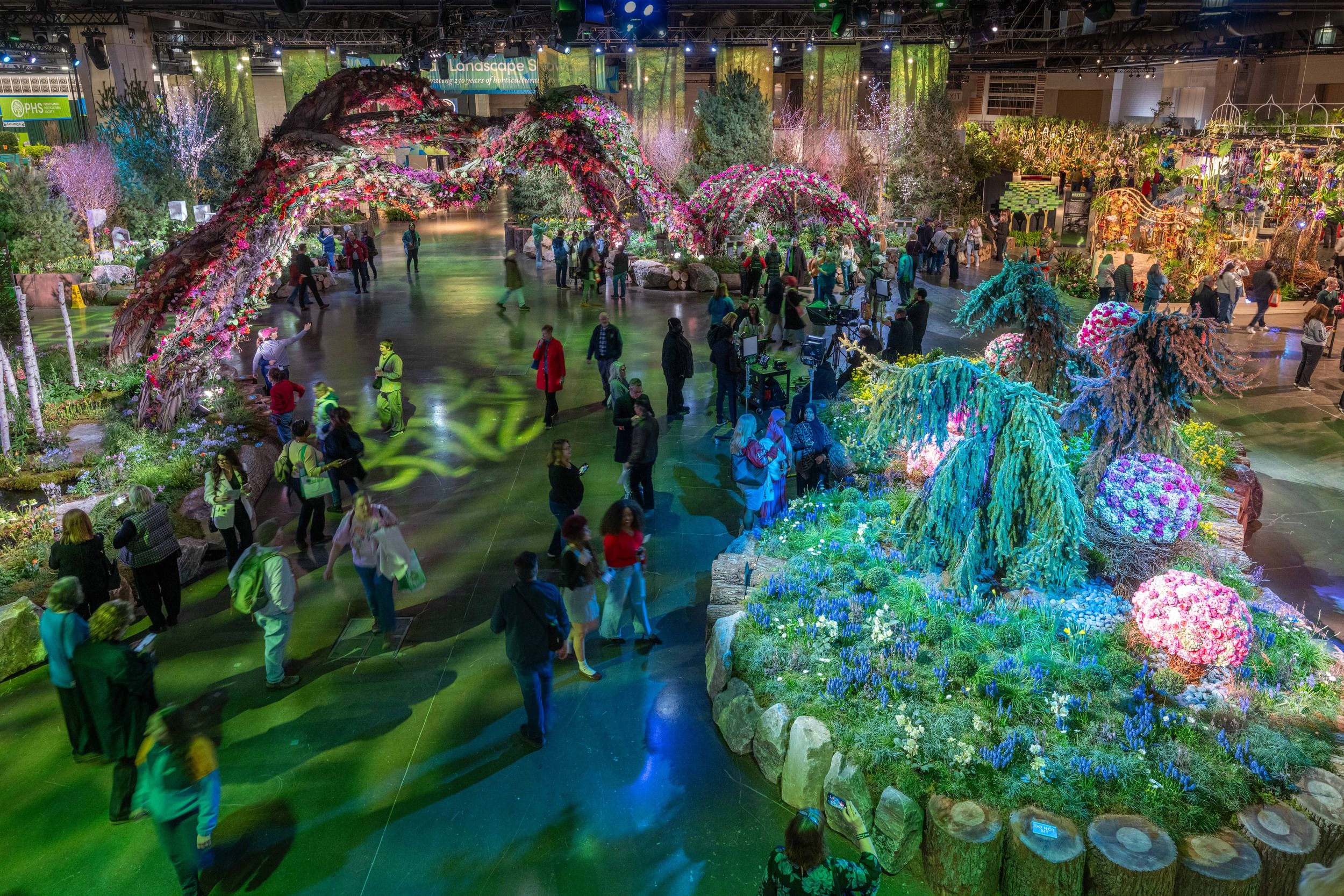 View from above of fanciful floral islands in a huge event hall, connected by sinuous arches of complex flower arrangements.