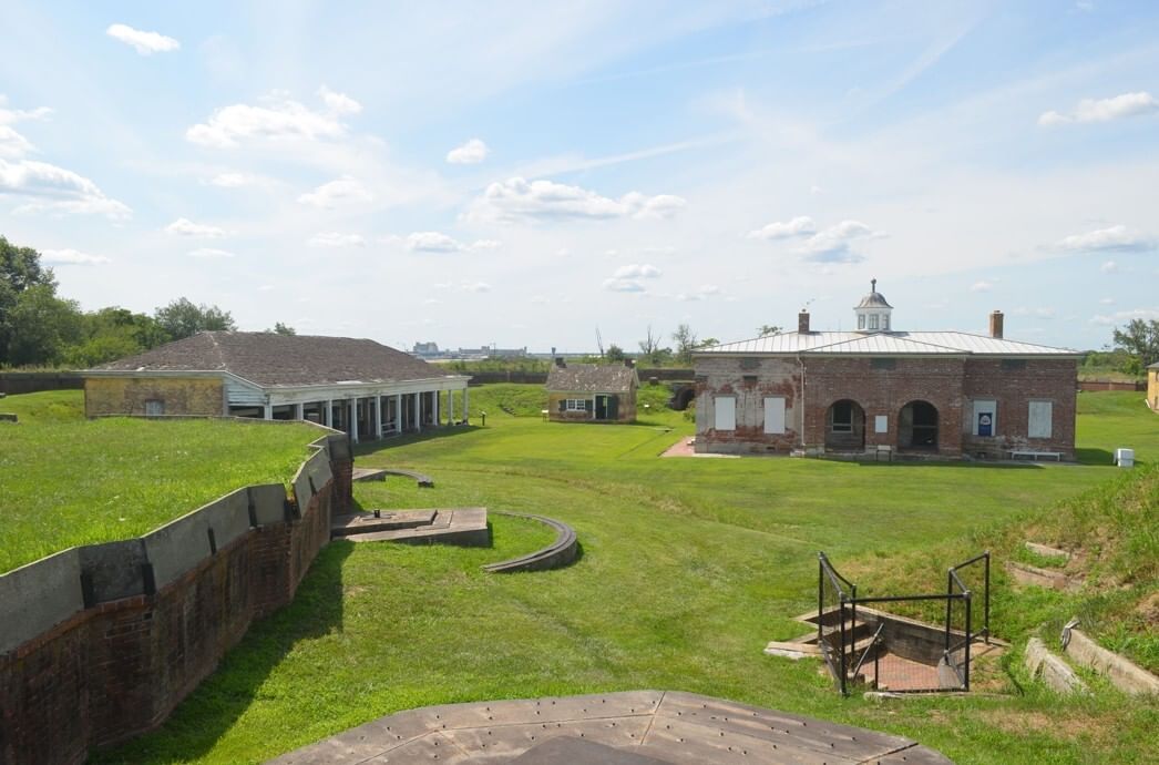 View of a small collection of 18th-century buildings & brick walls set into the landscape, with bright green grass in the sun