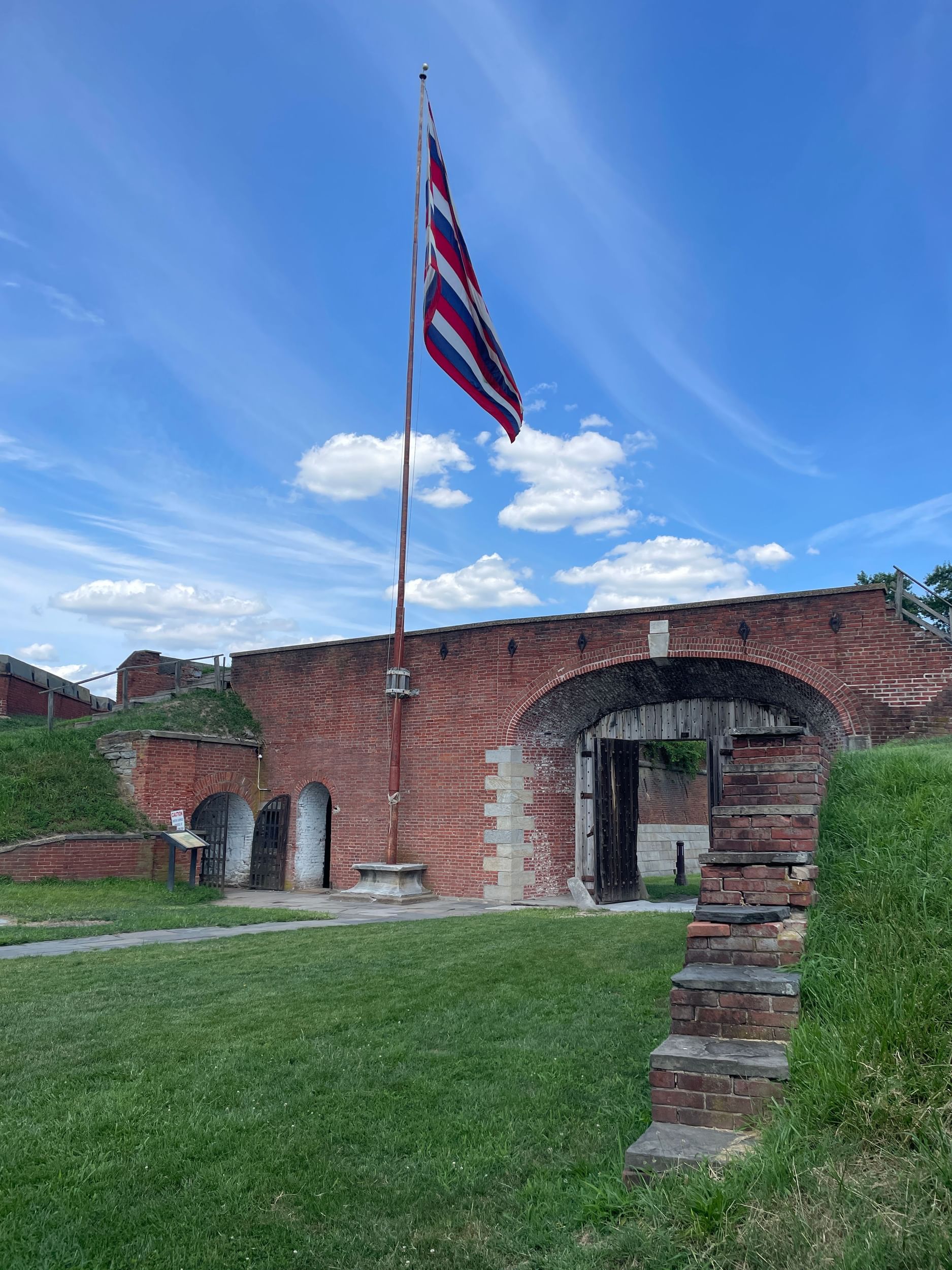 An entrance to Fort Mifflin with a thick brick archway built into the grassy hillside, under a red, white & blue striped flag