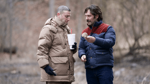 Robinson & Rudd, two white men outside in jackets, look at a mushroom that Rudd is holding.