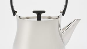 Close-up on a simple teapot in profile, made out of inviting matte silver metal with a gentle curving shape.
