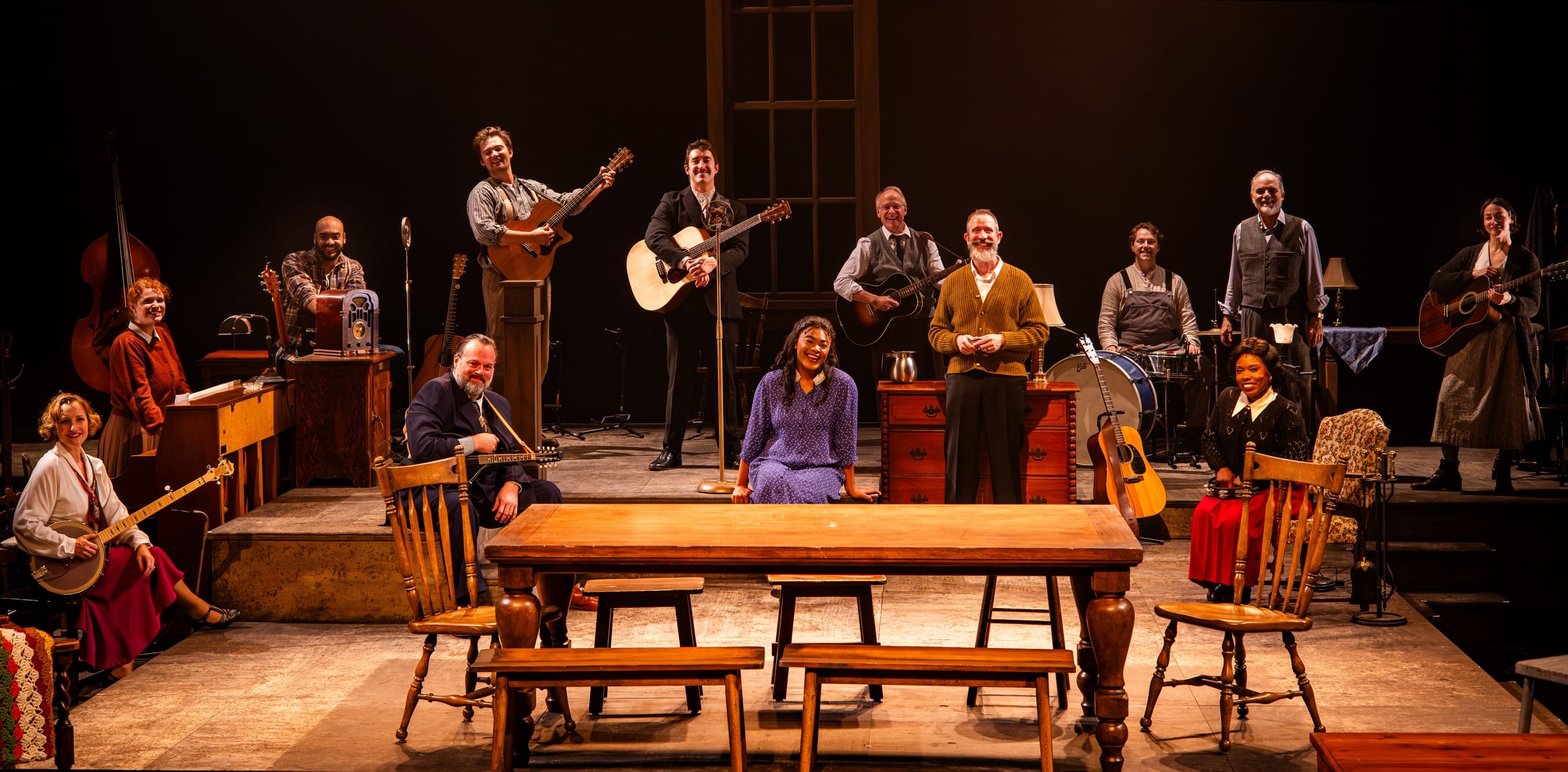13 actors of different races, genders, and ages, in 1930s garb, pose smiling with musical instruments across a large stage