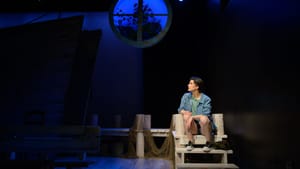 Looking plaintive, Feldman sits on a net-strewn dock on a darkened stage, a blue-lit round window above her head.