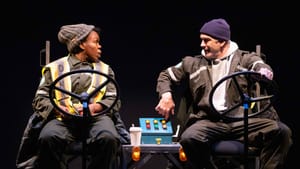 Ngozi Anyanwu and Steven Rishard in Garbologists. Costumed as sanitation workers, they talk inside the cab of a trash truck.