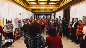 Gay and Landau, seen from behind, standing in front of a large crowd visiting the show in a gilded hallway of City Hall
