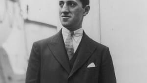 Black and white photo of Gershwin, a Jewish man in a black suit and tie, hand in pants pocket, looking to his left, outside