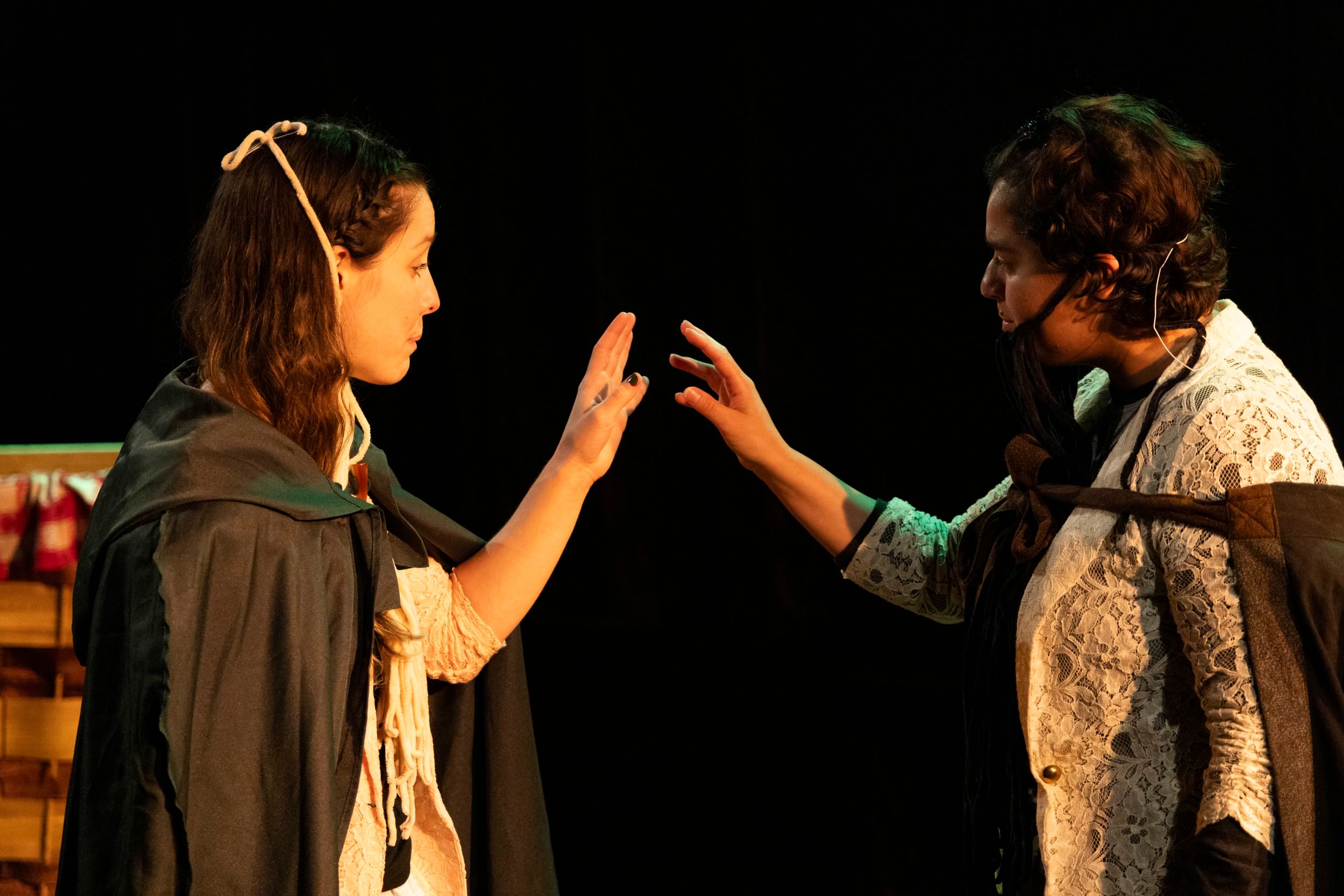 Two people wearing dark cloaks seen in profile, facing each other, each holding up a hand that almost touches the other