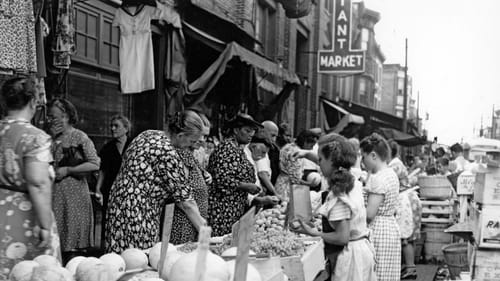 Children pack bags of varied fresh produce for the crowd of adults on the other side of the vendor tables.