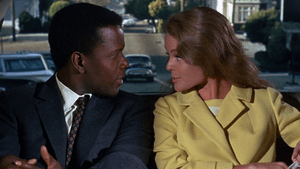 Movie still. Poitier and Katherine Hepburn sit close, looking at each other in a car, the road behind them.