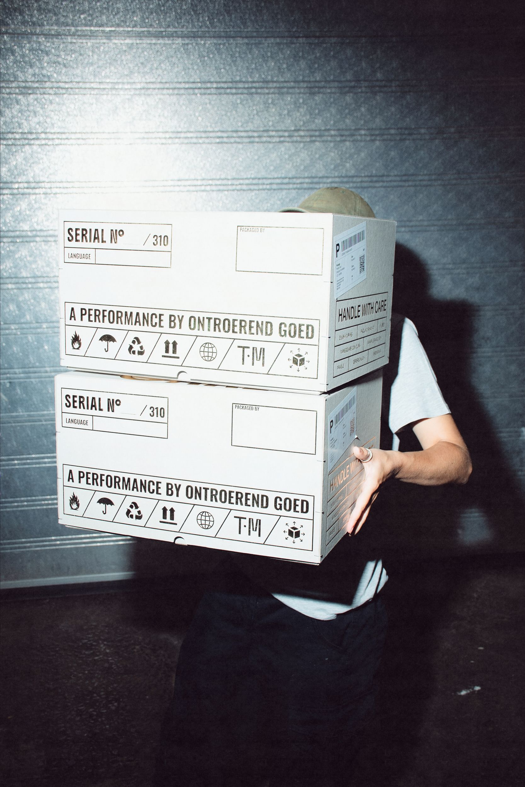A person carrying two large white boxes has their face hidden from them.