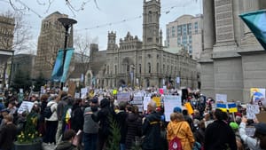 View over a crowd of thousands of protesters holding a sea of signs on a drizzly gray afternoon.