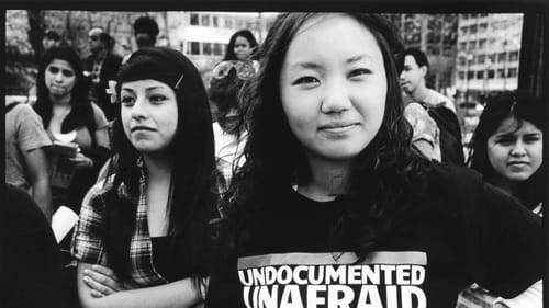 Black & white photo described below. A smiling Asian teenage girl poses confidently in a multiracial outdoor crowd.