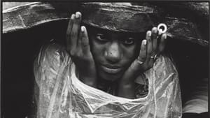 Finkle’s black & white photo, described in text below, of a Black woman sitting in the rain at a pro-housing protest.