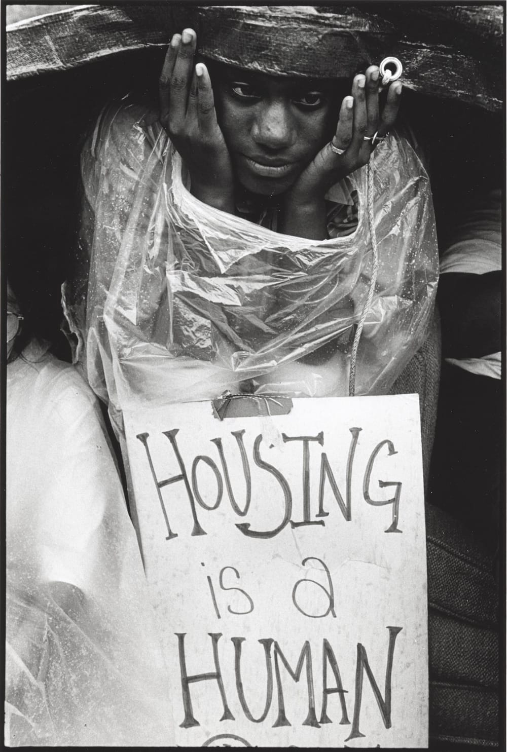 Finkle’s black & white photo, described in text below, of a Black woman sitting in the rain at a pro-housing protest.