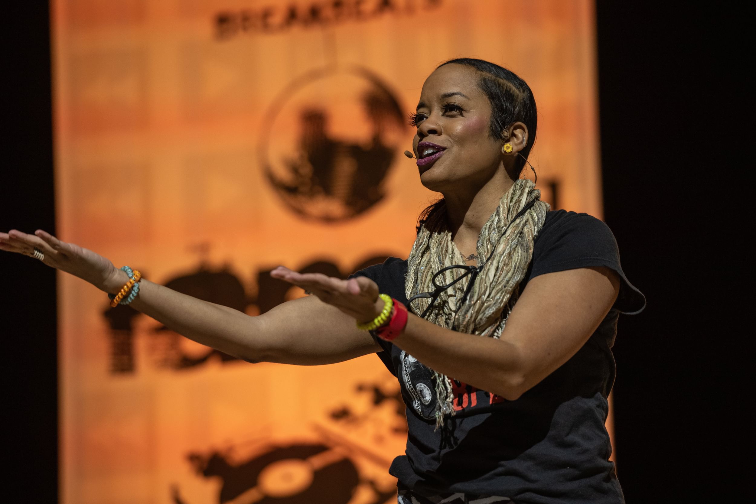 Actress Paige Hernandez on stage in casualwear, arms out and palms up, in mid-speech or -song on stage