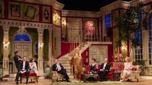 Eight people in 1920s evening wear sit on couches with various expression on a sumptuous, high-windowed living room set