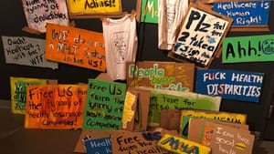Dozens of colorful hand-lettered protest signs with pro-healthcare slogans taped to a black wall at the theater.