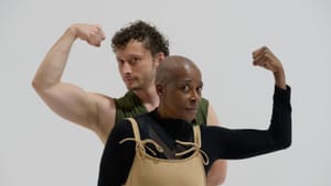 Grinberg, a white man, and Moore, a Black woman, strike a mirrored pose, standing close together with one bicep flexed.