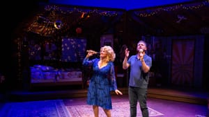 Paoluccio, dressed as Parton in a sparkly blue knee-length dress, sings onstage with Stern, wearing jeans and a polo.