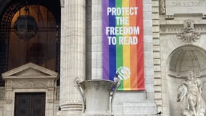 View of the grand stone entrance of the NYC Public Library, with a giant Pride flag with “Protect the Freedom to Read” on it.