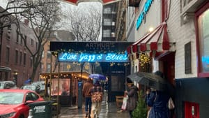Photo of a rainy New York City street and the red hanging sign for Marie’s Crisis Café, with ornate calligraphic lettering.