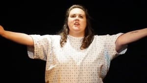 Snapp, a white woman with long brown hair, stands spreading her arms in a hospital gown.