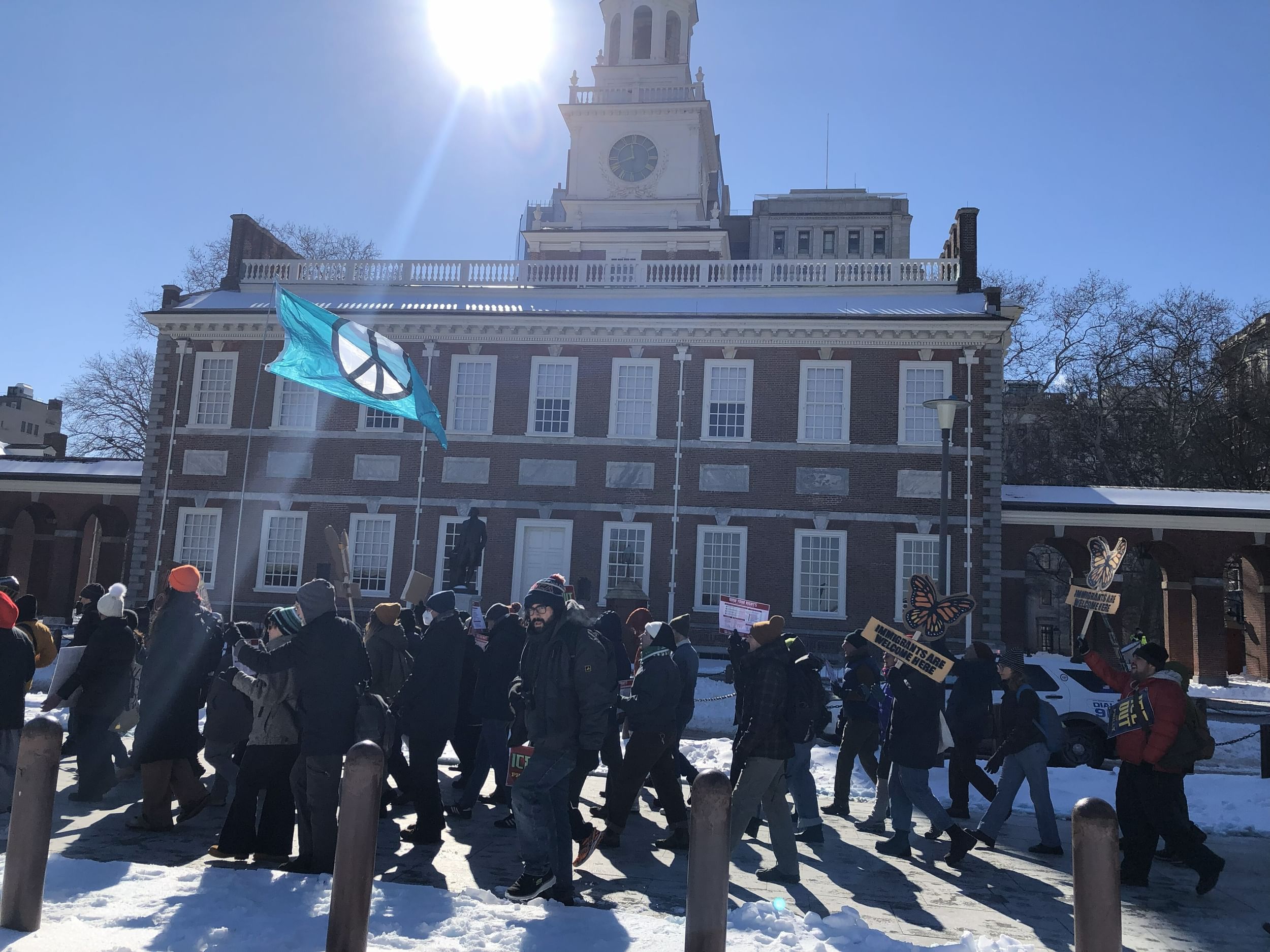 A few dozen marchers walk past historic Independence Hall on a bright winter day with snow on the ground.