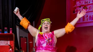 Carson dressed in pink tights, with a clear apron, flippers, and floaters on her arm. Arms out extended, exclaiming excitedly