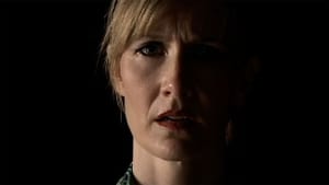 A screenshot of Dern looking towards the camera, half her face cast in shadows, pitch black behind her