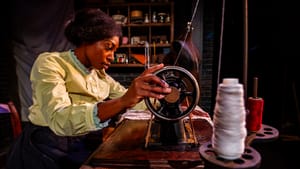 Porter, a Black woman working intently at a sewing table, seen from the side, hand on sewing machine wheel in the foreground