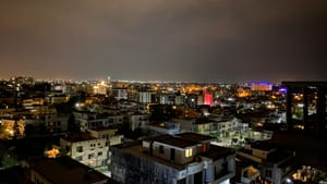 A nighttime city view in Islamabad, Pakistan, with dozens of boxy white buildings and colorful lights under a cloudy sky.