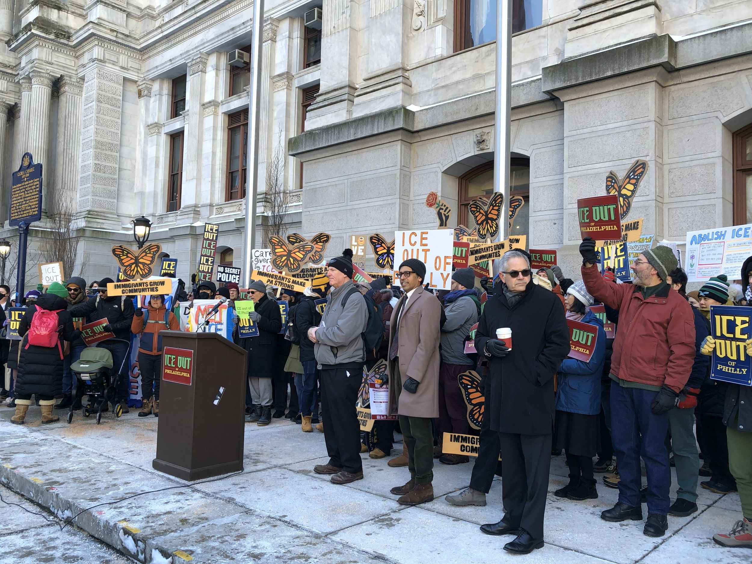 A few dozen people, many holding pro-immigrant signs, gather on a cold day at Philadelphia City Hall.