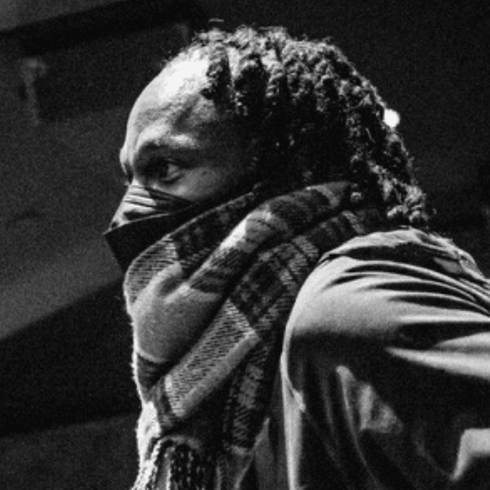Black & white photo of Page, a Black man wearing a facemask and a plaid scarf, seen in profile.