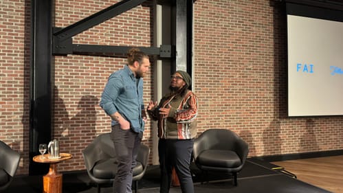 Krimes, a bearded white man in denim shirt, talks with Shirelle, a Black person in a striped jacket, glasses & gray cap.