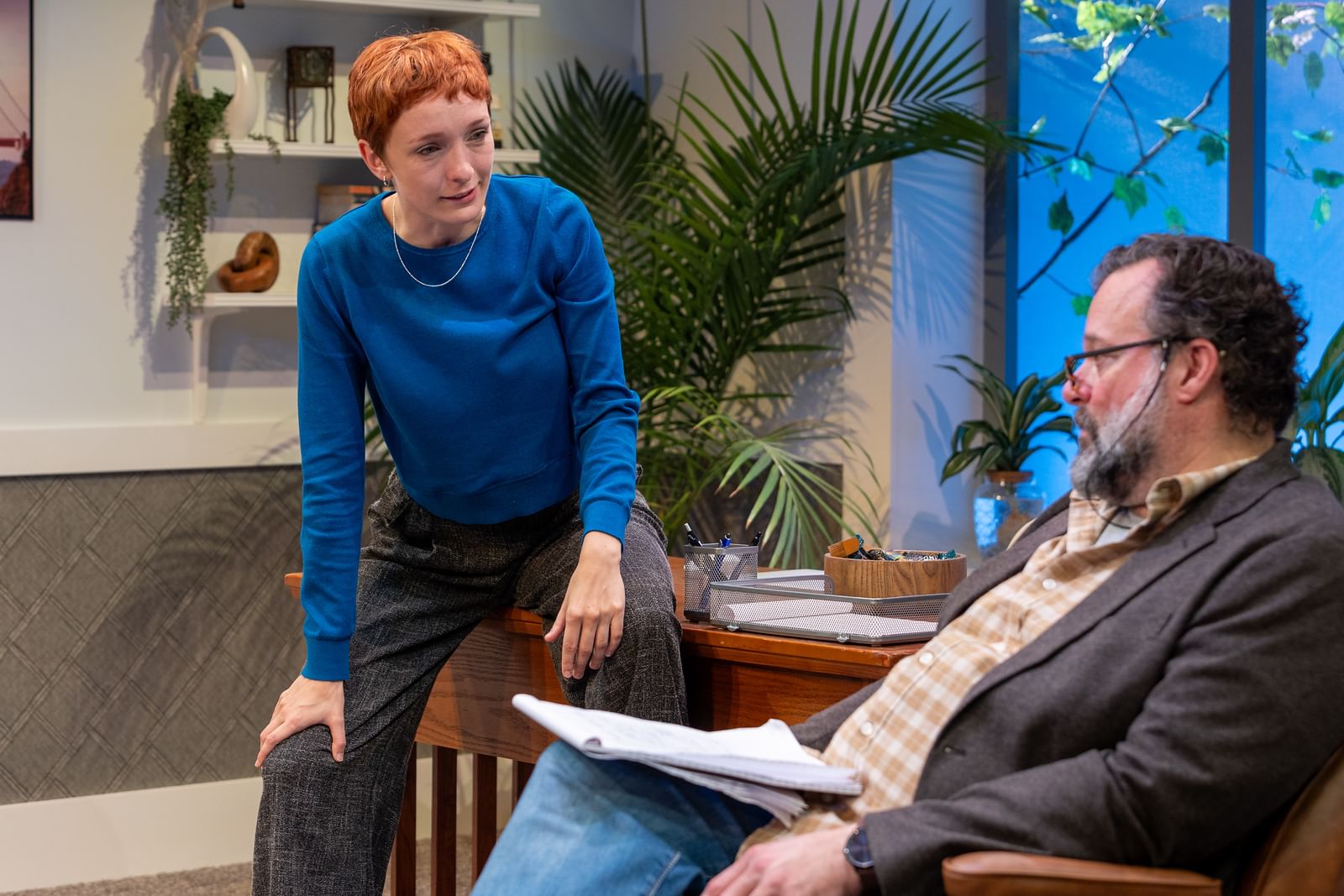 Gayle and Greer play a psychologist and his patient in an office with small art pieces and a large fern. They both look tired