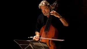 Savali plays a cello, a music stand in front of him, the background all black around him