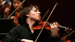 Close-up on Bell, a white man with short brown hair, playing his violin passionately with an orchestra.