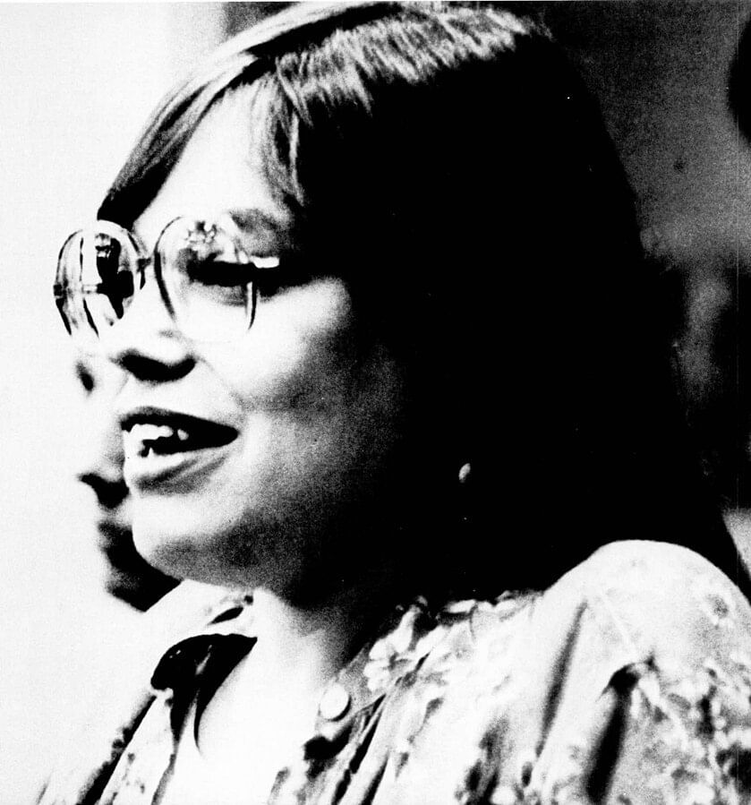 Black & white close-up on Heumann’s face: she is a smiling white woman with dark hair and large glasses