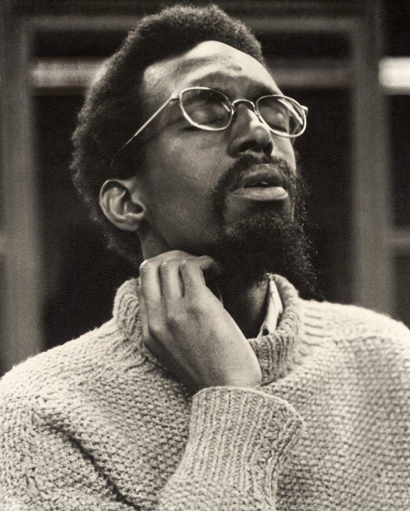 Vintage black & white photo of a young Eastman, a Black man with a beard and glasses, listening with a blissful expression.