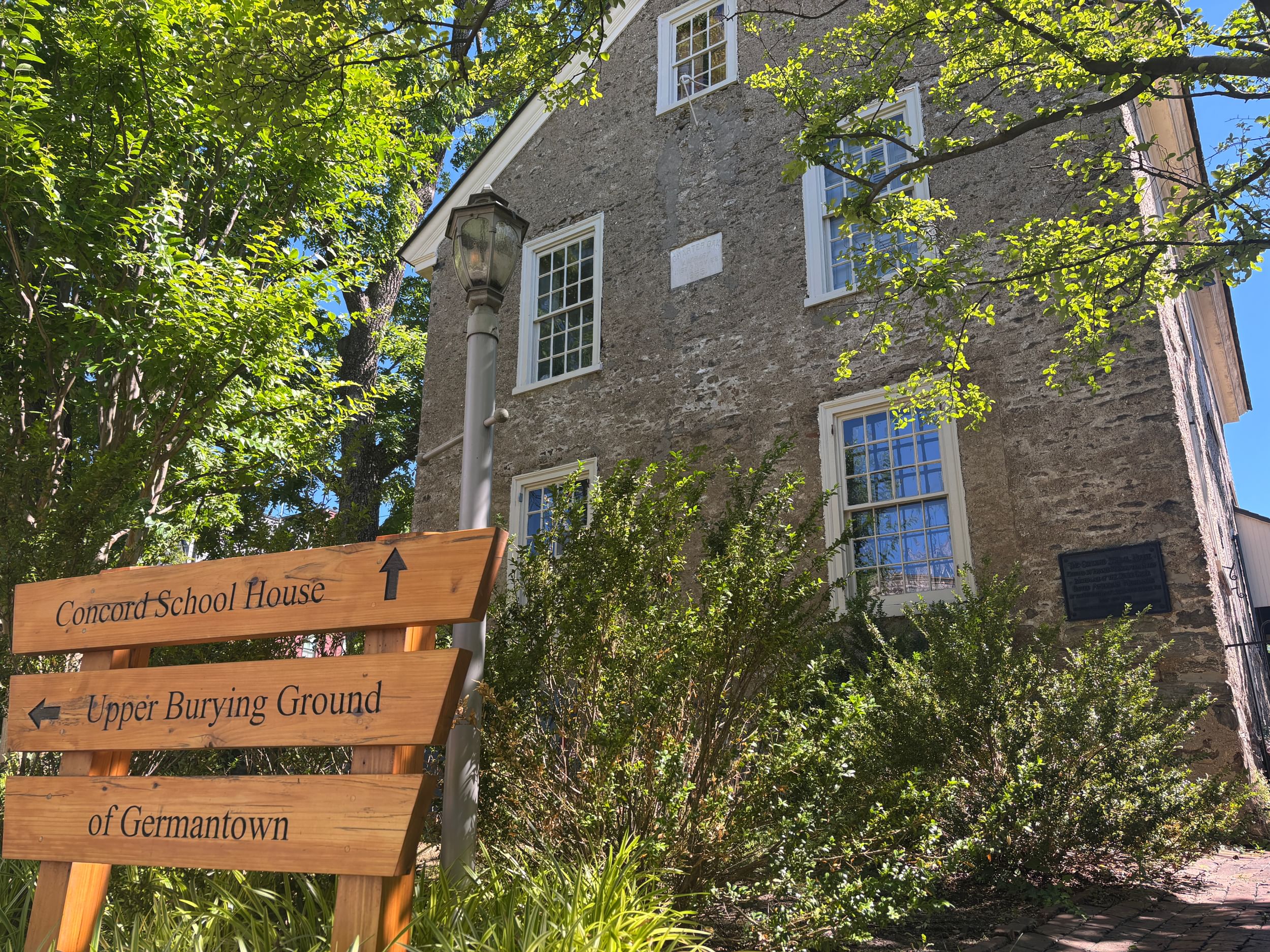 Closeup on one side of the schoolhouse, a three-story stone building built in 1775, surrounded by green summer trees.