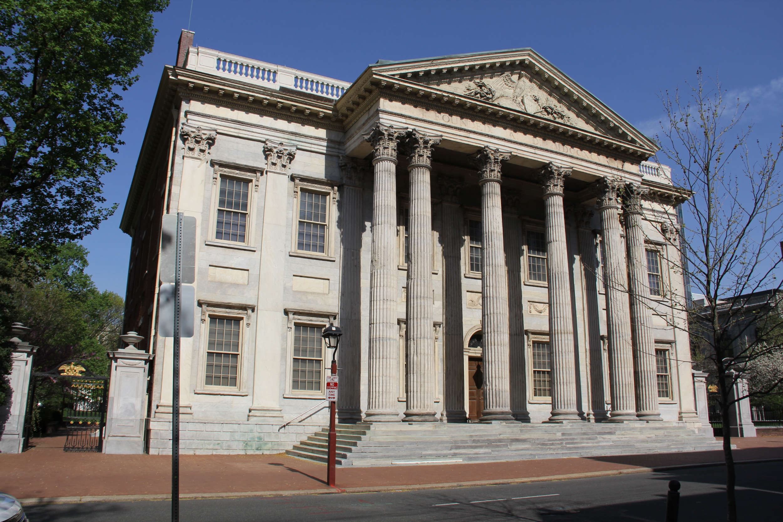 Large historic two-story stone building with grand windows and neoclassical columns, seen on a sunny day.