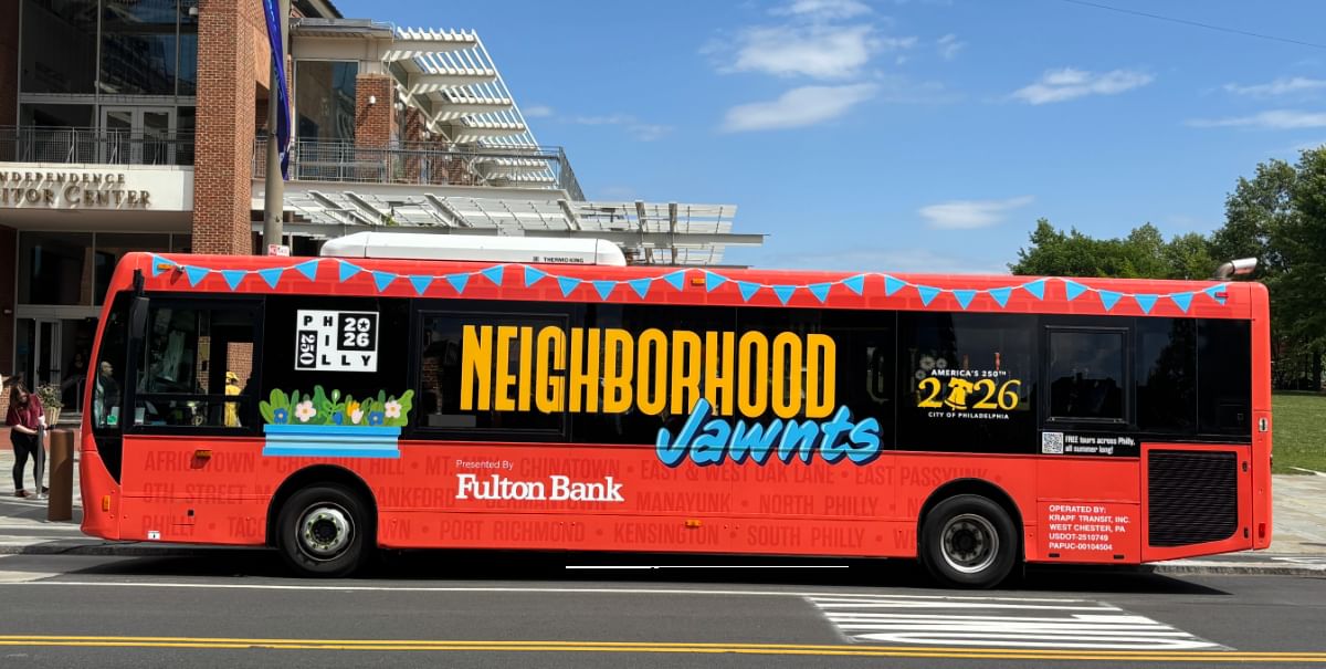 Long red tour bus with the huge yellow & blue JAWNTS logo parked by the Visitors Center on a sunny day.