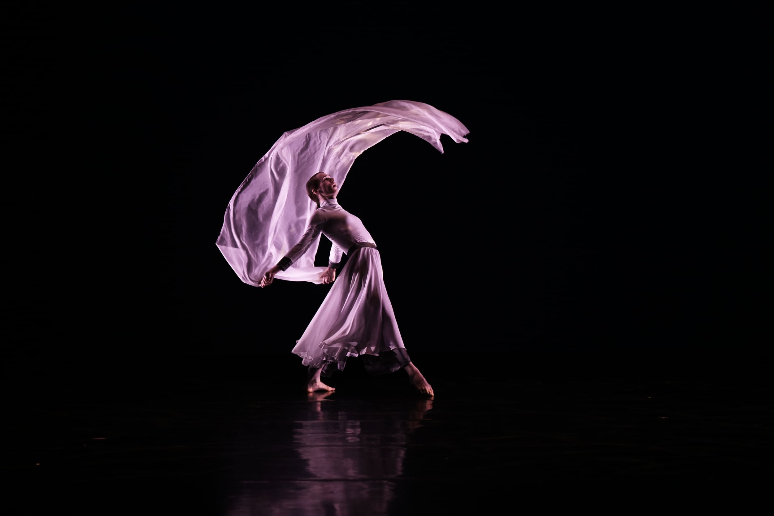 Niblett, in a flowing long-sleeve white dress, bends back gracefully and flips matching white fabric in a roof-like curve